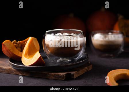 Tazza di latte di zucca speziato con panna montata e fette di zucca su sfondo di legno scuro. Foto Stock