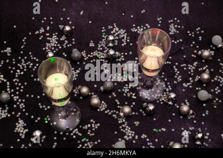Due bicchieri di champagne su sfondo scuro con palline decorative in argento e bianco e scintillanti tinelli in argento a forma di stelle. Romantico cre Foto Stock