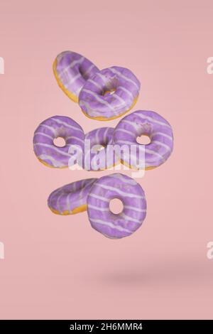 Ciambelle decorate in viola in movimento che cadono o volano su sfondo rosa. Dessert minimal e dolce concetto Foto Stock