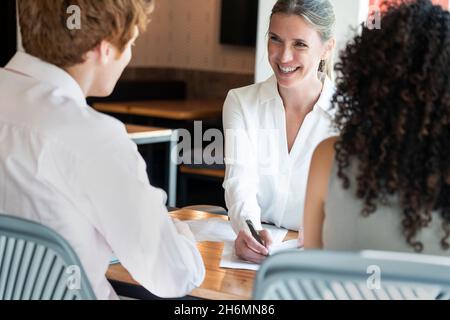 Donna matura sorridente che parla con la giovane coppia in ufficio Foto Stock