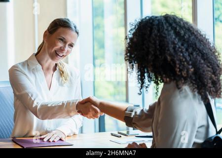 Donna matura sorridente che scuote le mani con la giovane donna in ufficio Foto Stock
