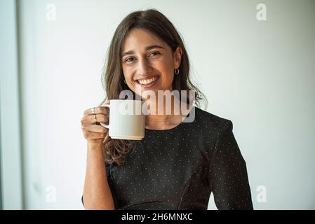 Ritratto di giovane donna sorridente che tiene una tazza di caffè Foto Stock