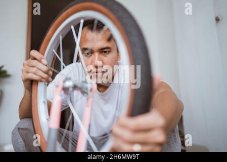 Papà asiatico mette su una ruota mentre si monta una bicicletta Foto Stock