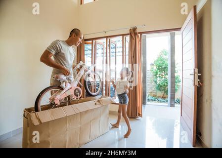 La figlia balla felicemente quando suo padre scollega una mini bicicletta Foto Stock