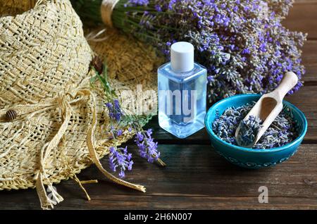 Cappello estivo in vimini con fiori freschi e secchi di lavanda e bottiglia di olio essenziale o acqua di lavanda per la produzione di cosmetici naturali. Foto Stock