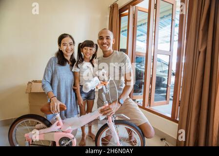 Sorridendo padre, madre e figlia asiatica che reggono una nuova mini-bike Foto Stock