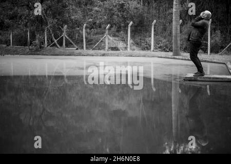 Scatto in scala di grigi di un uomo sconvolto coprendo il suo volto con le mani in piedi da una pozzanghera Foto Stock