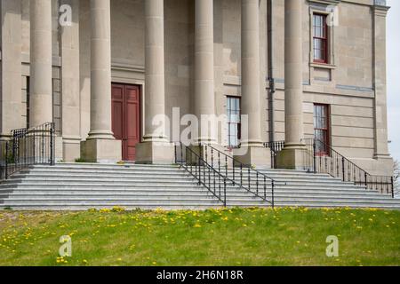 La facciata esterna di uno storico edificio governativo con grandi colonne o colonne di marmo vintage, porta rossa, binari neri e un'entrata in mattoni Foto Stock