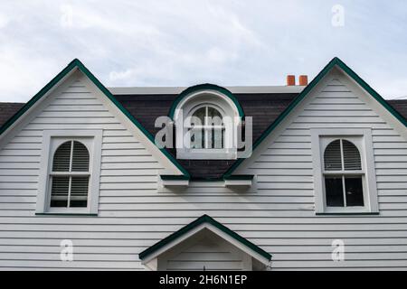 Una casa vintage in legno bianco con finestre multiple. La finestra centrale ha un dormer curvo sopra la finestra di vetro chiusa nel nero Foto Stock