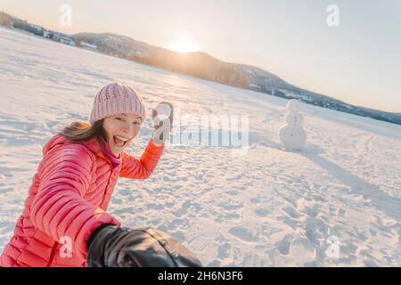 Inverno ragazza che lancia la palla di neve alla macchina fotografica sorridendo felice di divertirsi all'aperto in nevoso giorno d'inverno giocando nella neve. Bella giocosa multiculturale asiatico Foto Stock