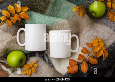 Due tazze bianche con soffice coperta di lana, mele verdi e foglie di giallo paglierino. Tazza vuota per la promozione del design, modello in stile Foto Stock