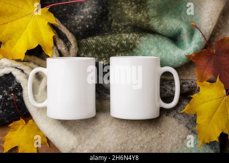 Due tazze bianche di caffè mockup con un'accogliente sciarpa di lana e foglie di acero caduta. Tazza vuota per la promozione del design, modello in stile Foto Stock