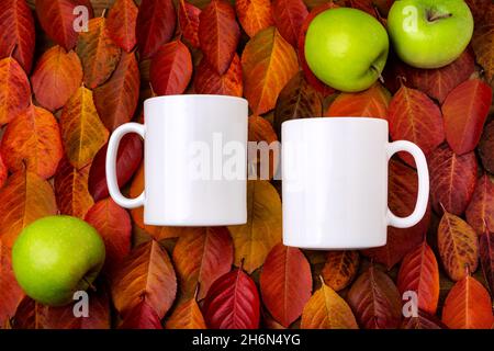 Due tazze bianche di caffè sulla caduta gialla rossa lascia mockup di fondo con tre mele verdi. Tazza vuota per la promozione del design, modello in stile Foto Stock