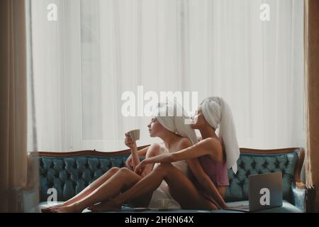 Belle ragazze che hanno la colazione a letto con un computer portatile in un hotel moderno. Gioiosa ragazza amici sdraiati a letto in soggiorno. Foto Stock