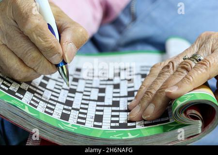 Immagine generica delle mani anziane femminili usando una penna per riempire un puzzle di cruciverba. Foto Stock
