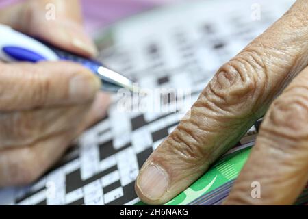 Immagine generica delle mani anziane femminili usando una penna per riempire un puzzle di cruciverba. Foto Stock