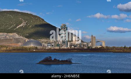 Vista di enorme cementificio industriale in Bow Valley vicino Canmore, Alberta, Canada nelle Montagne Rocciose nella stagione autunnale con il lago di fronte. Foto Stock