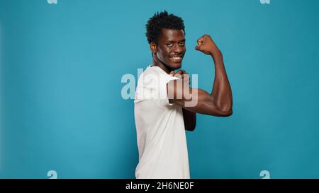 Persona atletica che flette i muscoli del bicipite sulla macchina fotografica in studio. Uomo addestrato che mostra muscolatura sulle braccia mentre si alza su sfondo isolato. Atleta con corpo muscolare dal fitness Foto Stock
