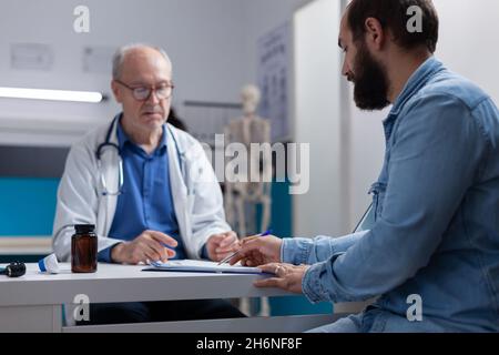 Paziente firma carte di controllo per la prescrizione su appuntamento medico con il medico. Giovane uomo che usa la penna per firmare documento di lavoro con assicurazione di consultazione e trattamento sanitario. Foto Stock