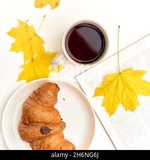 croissant con caffè sullo sfondo di un mucchio di libri. Studente che mangia la colazione, concetto di studio. Foto Stock