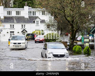I veicoli percorrono una strada allagata a Waterhead, Ambleside, Lake District, Regno Unito, dopo piogge torrenziali che hanno portato il lago Windermere a raggiungere livelli molto elevati Foto Stock
