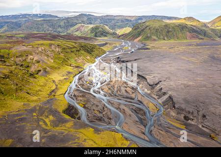 Fiume con diramazioni soffocate attraverso sabbia di lava nera, paesaggio di montagna sovrastato da muschio, ghiacciaio di Hoefoabrekkajoekull sullo sfondo Foto Stock