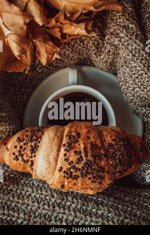 Una tazza di caffè nero del mattino con un croissant al cioccolato. Pasto delizioso. Estetica nei dettagli. Tonalità accoglienti beige e marrone Foto Stock