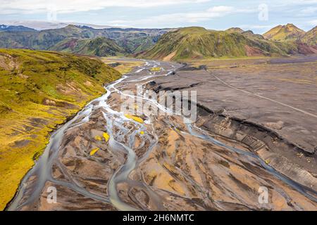 Fiume con diramazioni soffocate attraverso sabbia di lava nera, paesaggio di montagna sovrastato da muschio, ghiacciaio di Hoefoabrekkajoekull sullo sfondo Foto Stock