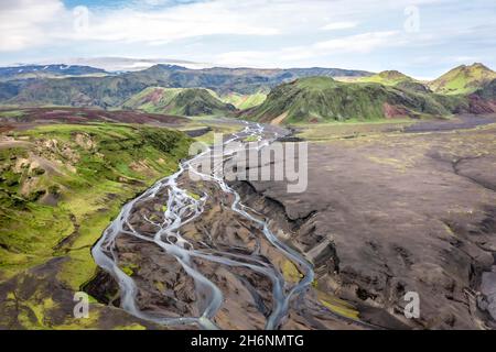 Fiume con diramazioni soffocate attraverso sabbia di lava nera, paesaggio di montagna sovrastato da muschio, ghiacciaio di Hoefoabrekkajoekull sullo sfondo Foto Stock