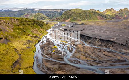 Fiume con diramazioni soffocate attraverso sabbia di lava nera, paesaggio di montagna sovrastato da muschio, ghiacciaio di Hoefoabrekkajoekull sullo sfondo Foto Stock