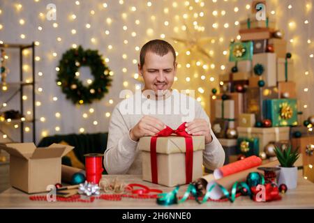 Felice giovane uomo che lega un arco in regalo a casa Foto Stock