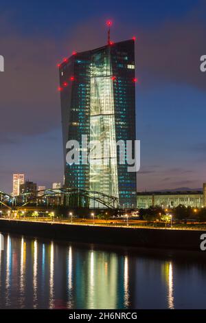 Banca centrale europea illuminata, la BCE si è riflessa nel fiume meno durante il tramonto tardivo da Arthur-von-Vineyard-Steg, Francoforte sul meno, Assia, Germania Foto Stock