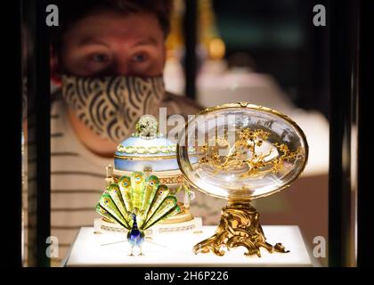 Un dipendente del museo guarda una vetrina contenente l'uovo di pavone (primo piano) e il Cradle with Garlands Egg (sfondo) durante una telefonata per la prossima mostra del Victoria and Albert Museum 'Faberge a Londra: Romance to Revolution'. Data foto: Mercoledì 17 novembre 2021. Foto Stock