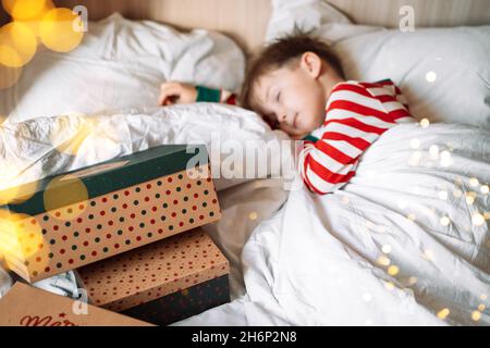 Ragazzo che dorme su biancheria da letto bianca accanto ai regali di natale Foto Stock