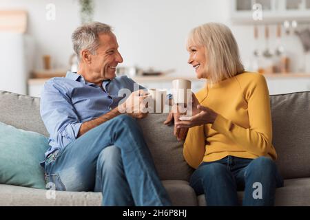 Coppia matura allegra che beve il tè e parla seduto a casa Foto Stock