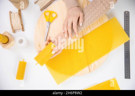 Donna artigiana che fa candele da cera d'api gialla con le mani, vista dall'alto. Foto Stock