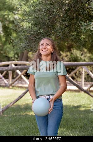 Donne caucasiche di mezza età che indossano t-shirt e jeans gioca con una palla nel parco, tre quarti di colpo Foto Stock