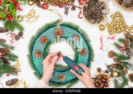 Facendo una grande corona di Natale passo dopo passo, passo 5 - colla a caldo i coni di pino Foto Stock