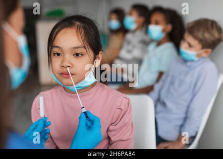 Asian Preteen Girl Getting testato per Covid-19 seduta in clinica Foto Stock
