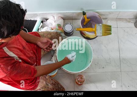 Mano che mescola vernice verde in un secchio di plastica Foto Stock