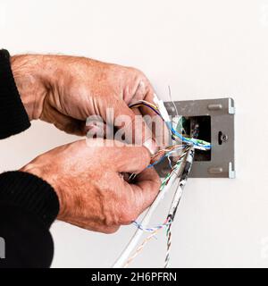 Le mani di un anziano montano una rosetta in una parete bianca. Riparazione dell'appartamento. Internet Foto Stock