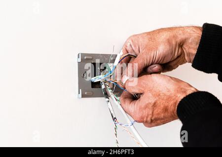 Le mani di un anziano montano una rosetta in una parete bianca. Riparazione dell'appartamento Foto Stock