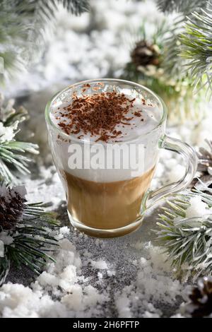 Latte macchiato di Natale. Una grande bevanda calda al caffè con scaglie di cioccolato, tra i rami di pino innevato e la neve. Foto Stock