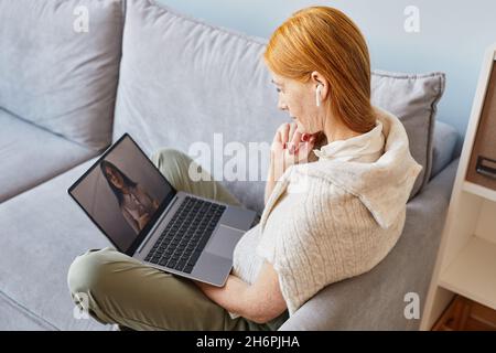 Ritratto laterale di giovane donna dai capelli rossi usando il laptop mentre studia in linea a casa Foto Stock
