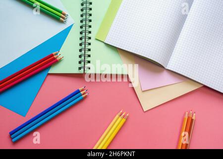 Concetti di scuola e hobby. Fogli di carta colorati, matite colorate e notebook su sfondo di carta rosa. Spazio di copia Foto Stock