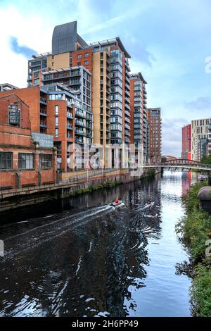 Spinningfields, Manchester. Nuovi ed eleganti edifici sul fiume Irwell. Un vogatore viene allenato da un uomo in una piccola barca. Foto Stock