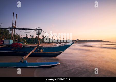 Barca da pesca sulla spiaggia di sabbia all'alba colorata. Litorale vicino a Tangalle in Sri Lanka Foto Stock