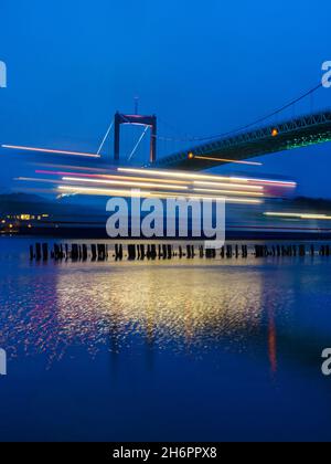 Traghetto che passa il ponte alla luce della sera Foto Stock