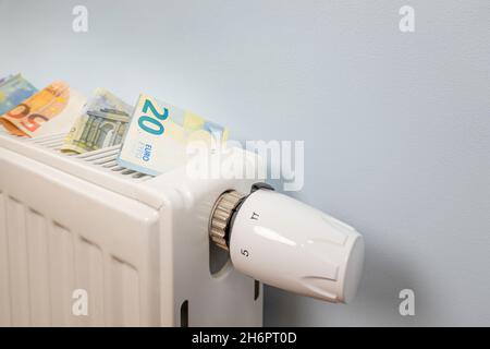 Costi di riscaldamento costosi. Pagamento delle fatture. Banconote in euro sulla batteria del radiatore di riscaldamento con regolatore di temperatura a casa Foto Stock