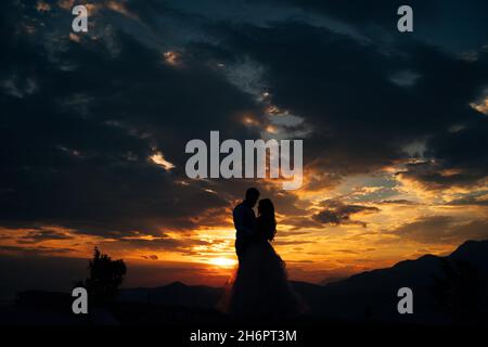 Silhouette della sposa e dello sposo che stanno abbracciando sopra Monte Lovcen con vista sulla Baia di Cattaro al tramonto Foto Stock